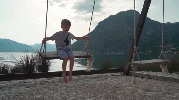A Boy Swing on a Swing Near the Sea with a Beautiful View of the Bay and Mountains