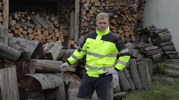 Lumberjack in Reflective Jacket. Man Woodcutter Hold Huge Axe Show Ok Sign. Sawn Logs, Firewood