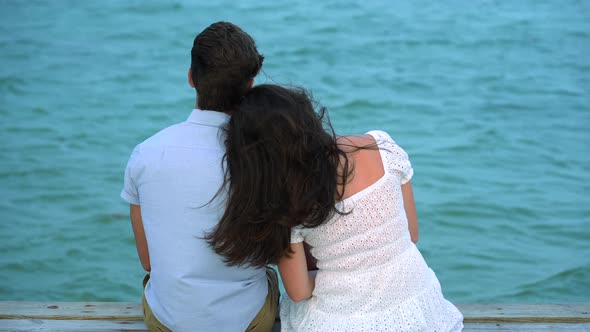 Close up of young couple in love sitting on ocean dock with turquoise tropical ocean waters.