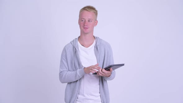 Happy Young Blonde Handsome Man Thinking While Using Digital Tablet