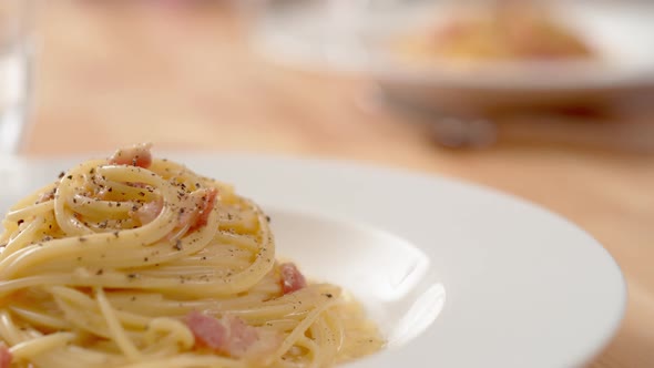 Camera follows carbonara pasta being served on table. Slow Motion.