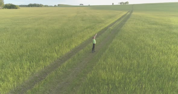 Sporty Child Standing in Green Wheat Field with Raised Hands Up