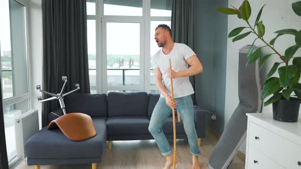 Man Cleaning the House and Having Fun Dancing and Singing with a Broom