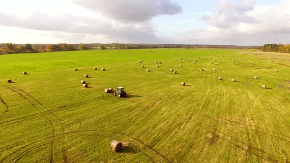 The tractor is stacking haystacks on an agricultural field in autumn, aerial view