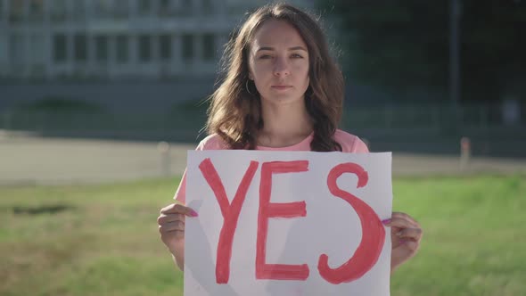 Portrait of Young Brunette Woman Holding Yes Poster Outdoors. Serious Female Caucasian Activist