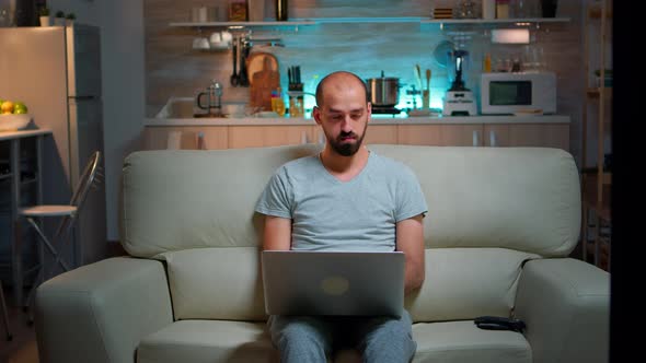 Focused Man Sitting on Sofa and Writing Online Project on Laptop