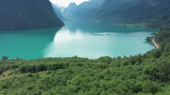 Green lush forest and glacier green freshwater lake in Olden Norway - Aerial flying over forest and