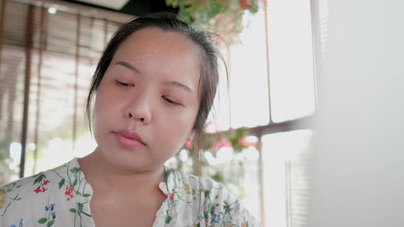 Face close up freelancer Asian woman scooping the delicious cake and using laptop in coffee shop