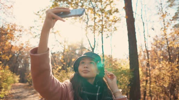 Charming Girl Is Taking Selfie By Mobile Phone in Sunny Autumn Forest, Smiling