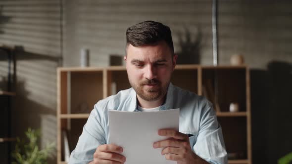 Handsome Young Caucasian Man Looking Through Paper Correspondence at Home Office Reading Letter with