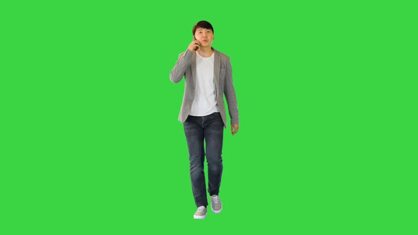 Young Asian Man Walks Talking on His Smartphone and Smiling on a Green Screen Chroma Key