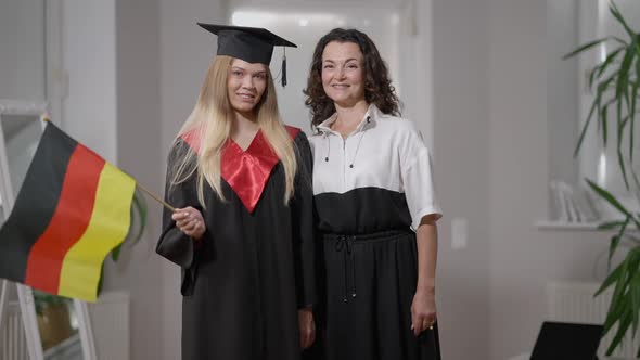 Medium Shot Portrait Glad Caucasian Mother and Daughter in Graduation Outfit Posing with German Flag