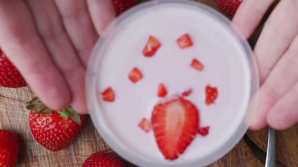 Woman Puts a Bowl of Strawberry Yogurt on the Dining Table with Her Hands. The View From the Top