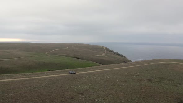 Aerial Around View Shot High Speed Suv Car Driving on Top of Mountain Road Natural Sky Seascape