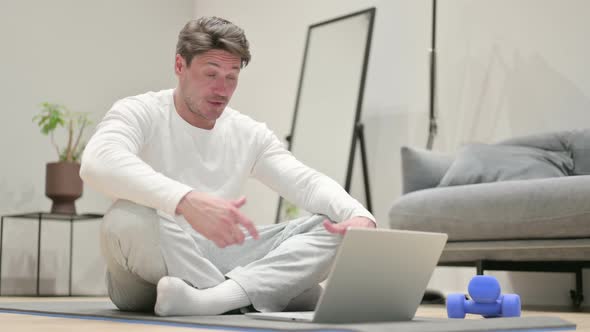 Middle Aged Man Talking on Video Call on Laptop While on Yoga Mat