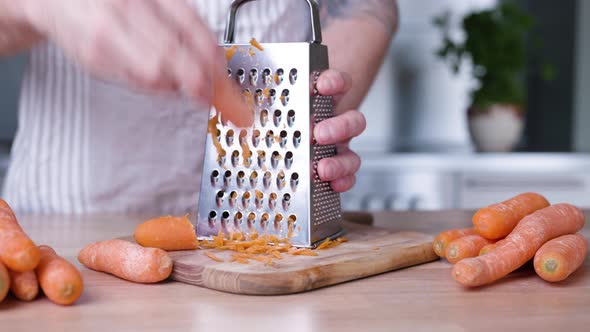 Man Grating Fresh Carrots On Grater For Baking A Delicious Carrot Cake. - close up