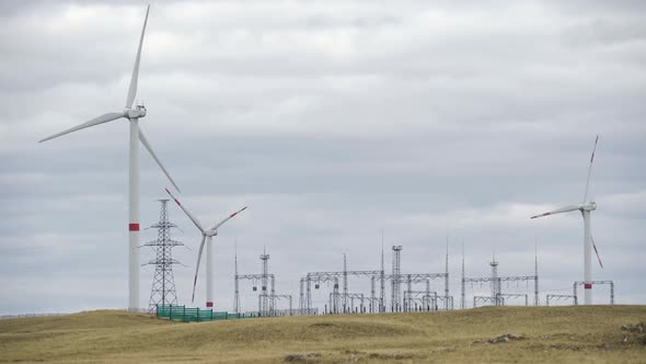 Motion the Blades of a Large Wind Turbine in a Field Against a Background of Cloudy Grey Sky on the