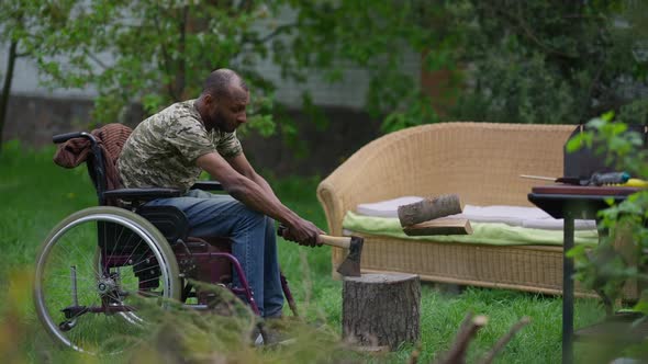 Side View Wide Shot of Disabled Man in Wheelchair Chopping Wood with Ax Outdoors on Backyard