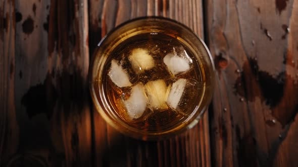 Close-up of Full Glass of Whiskey with Ice Slowly Rotates on a Black Background.