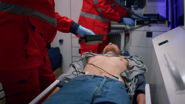 Emergency Medical Doctors Using Heart Defibrillator on Patient in Ambulance Car