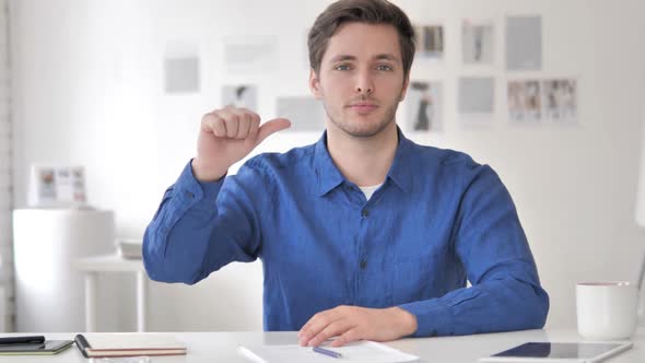 Thumbs Down By Casual Adult Man Sitting at Workplace