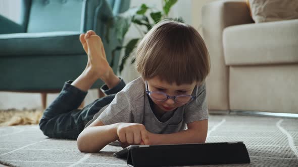 Child Using Tablet Lying on the Floor at Home Entertainment and Playing Online Games