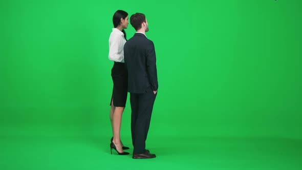 Couple of Young People in Suits Man and Woman Stand in the Green Space of the Chromakey Watching and