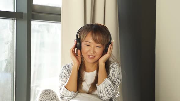 Beautiful Japanese Woman Listening To Music in Bed Woman Enjoying a Day Off