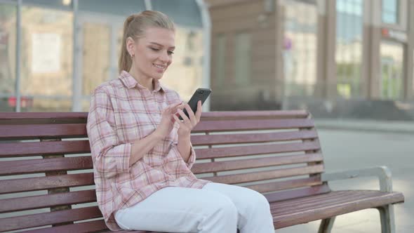Young Woman Using Smartphone While Sitting Outdoor on Bench