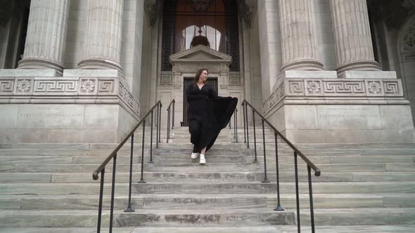 Girl in a long black dress runs down the stairs at entrance to New York library.