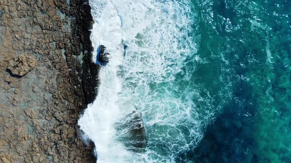 Sea Washes the Rocky Shore Above Aerial Shot Flying Over Coastline Cliffside with Blue Pure Water