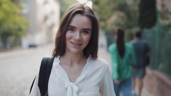 Portrait of Pretty Brunette Student Girl with a Bag Looking To Camera with a Smile. Young Woman