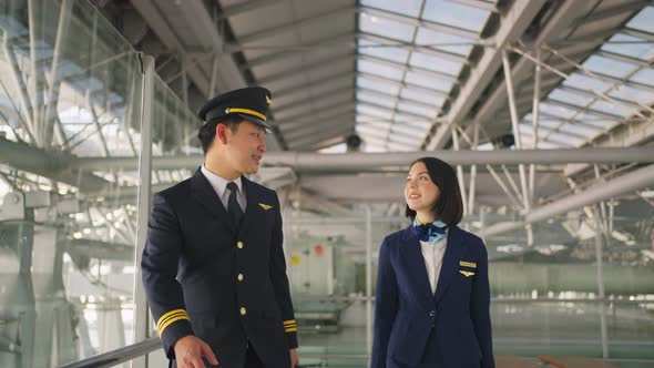 Asian airliner pilot and air hostess walking and talking together in airport terminal to airplane.