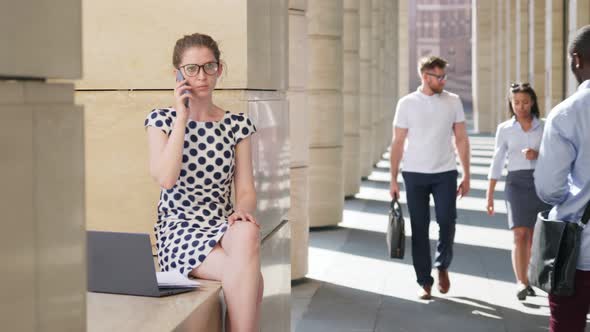 Young Businesswoman Having Phone Call Working on Laptop Sitting Outdoors Downtown