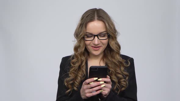 Young Smiling Woman Texting on Her Phone on Gray Background in Studio