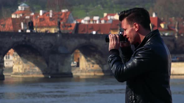 A Young Handsome Man Takes Photos of a Quaint Town with a Camera - a Bridge Over a River