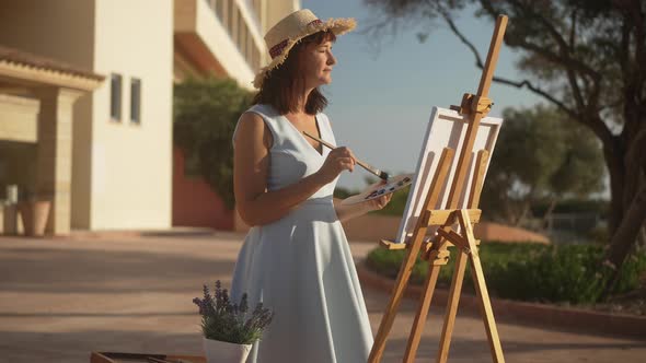 Talented Inspired Caucasian Woman Looking at Landscape at Sunrise Painting Picture on Canvas in