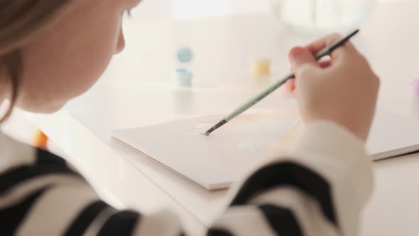 Little kid girl artist drawing coloring picture with paints and brushes.