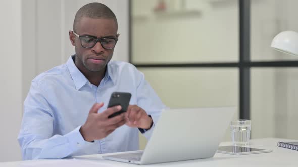 African Man Using Smartphone and Laptop for Work