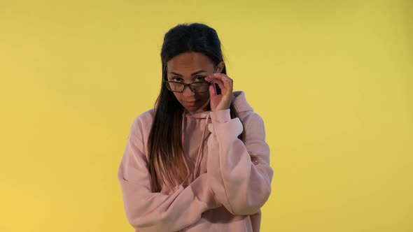 Multiethnic Young Woman Looking Over Her Glasses on Yellow Background