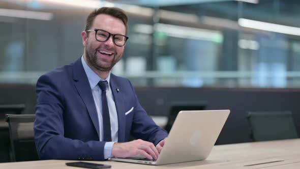 Middle Aged Businessman with Laptop Smiling at Camera