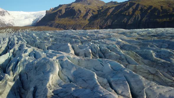 Aerial view over a icy glacier texture, towards a sunlit mountain in Iceland