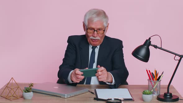 Worried Senior Businessman Sits at Workplace Avoid Working and Playing Racing or Shooter Video Games