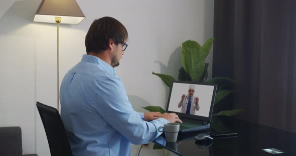 Senior Male Doctor Wears White Medical Coat, Stethoscope, Headset Makes Distant Video Call. Old