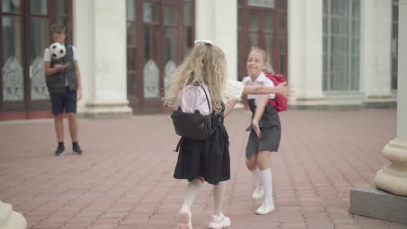 Cute Girl Running and Hugging Classmate After School Holidays. Blurred Boy Standing with Soccer Ball