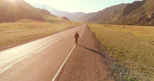 Flight Over Hitchhiker Tourist Walking on Asphalt Road. Huge Rural Valley at Summer Day. Backpack