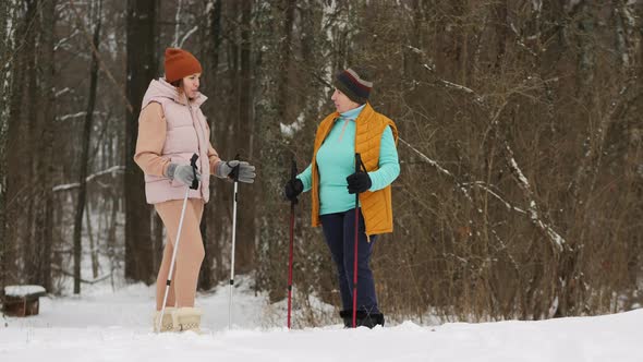 A Young Woman Trainer Explains To an Elderly Woman the Technique of Nordic Walking in a Snowy Forest