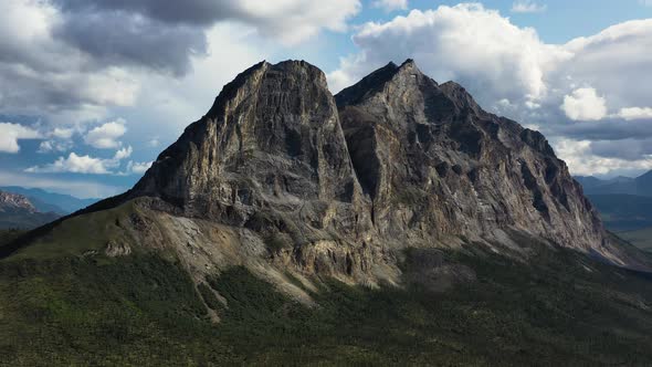 Orbiting aerial shot of famous Sukakpak Mountain against white clouds in summer Alaska without snow