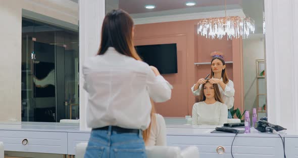 Hairdresser Combing Hair to a Girl in a Beauty Salon in Front of a Large Mirror