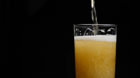 Beer is pouring into glass with foam sliding down side of beer glass